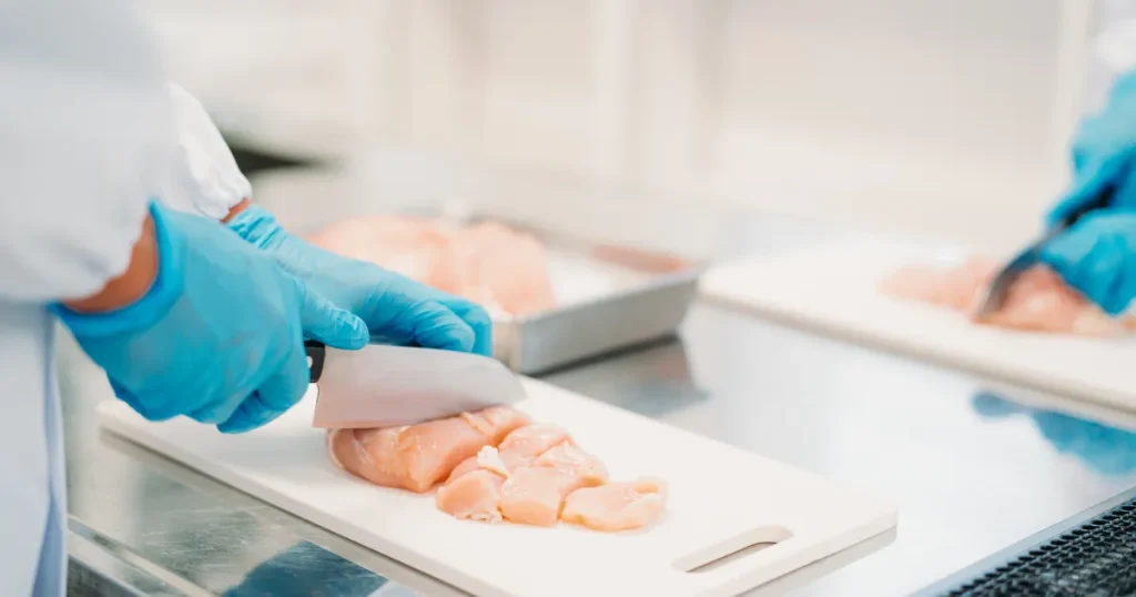 食品加工の現場で、青い手袋を着用したスタッフが鶏肉を丁寧にカットしている様子。