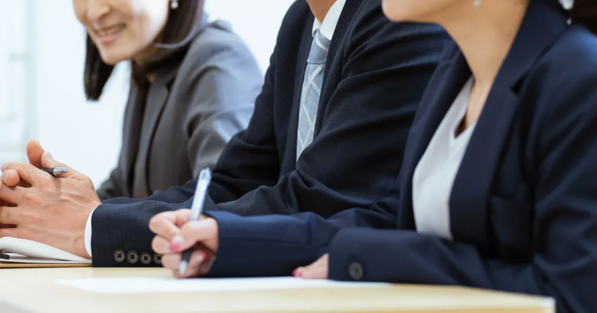 就職面接で逆質問を問われる理由を説明するセクションのイメージ。スーツ姿でメモを取る面接官たちの手元。