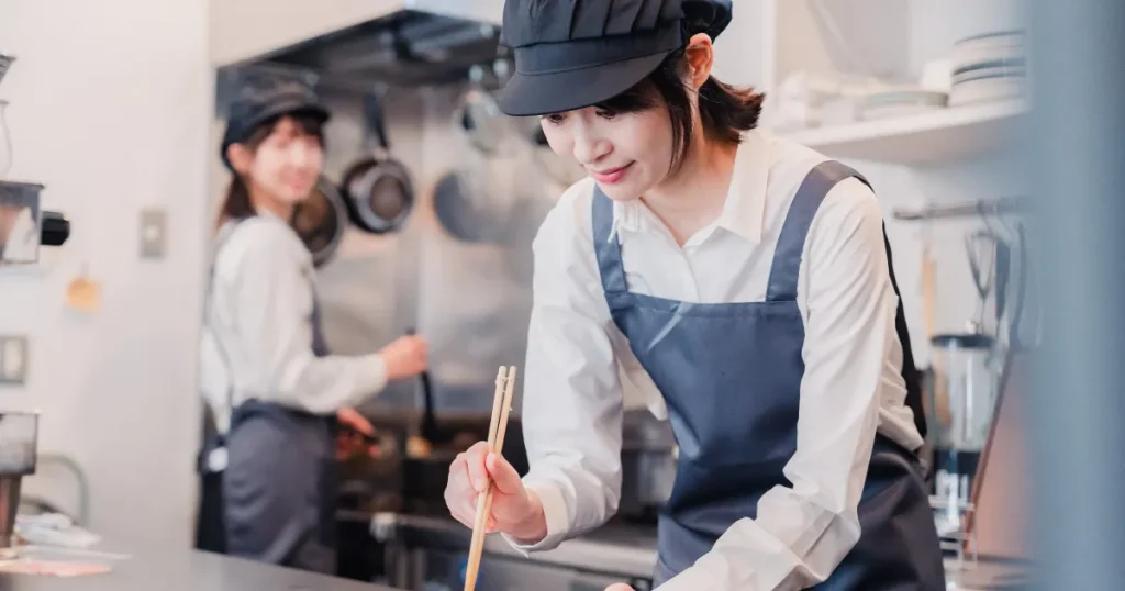 キッチンで調理作業をしている女性スタッフ。清潔な制服を着用し、調理や盛り付けに集中する姿が印象的。