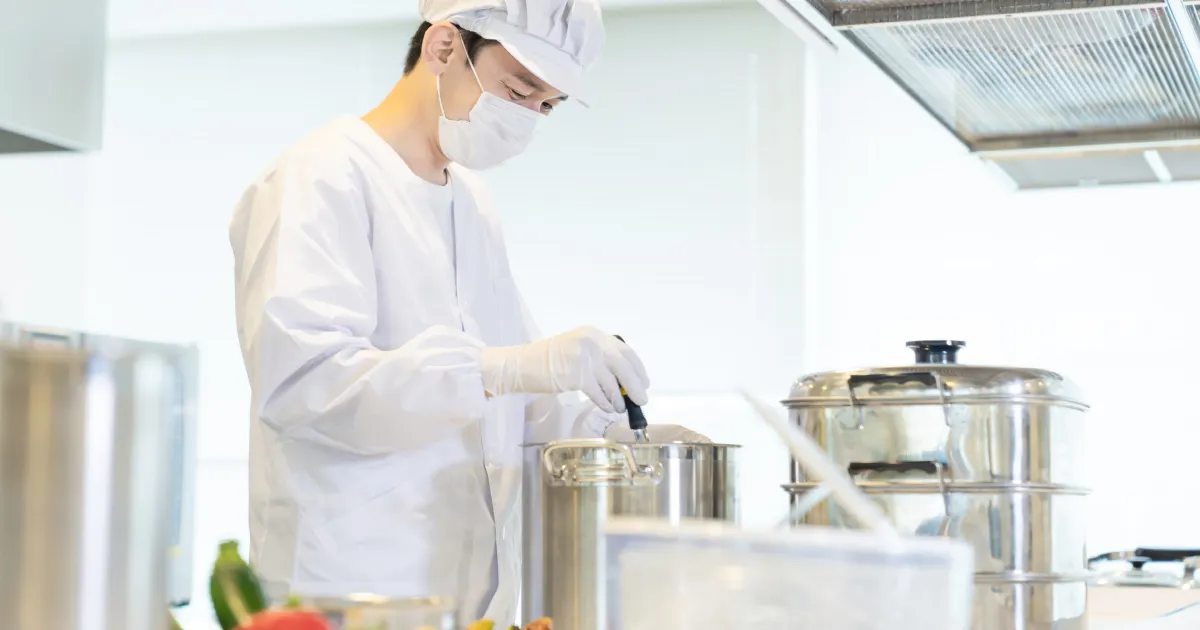 清潔な白衣とマスクを着用し、調理場で真剣に作業をする男性スタッフ。衛生管理が徹底された調理現場。