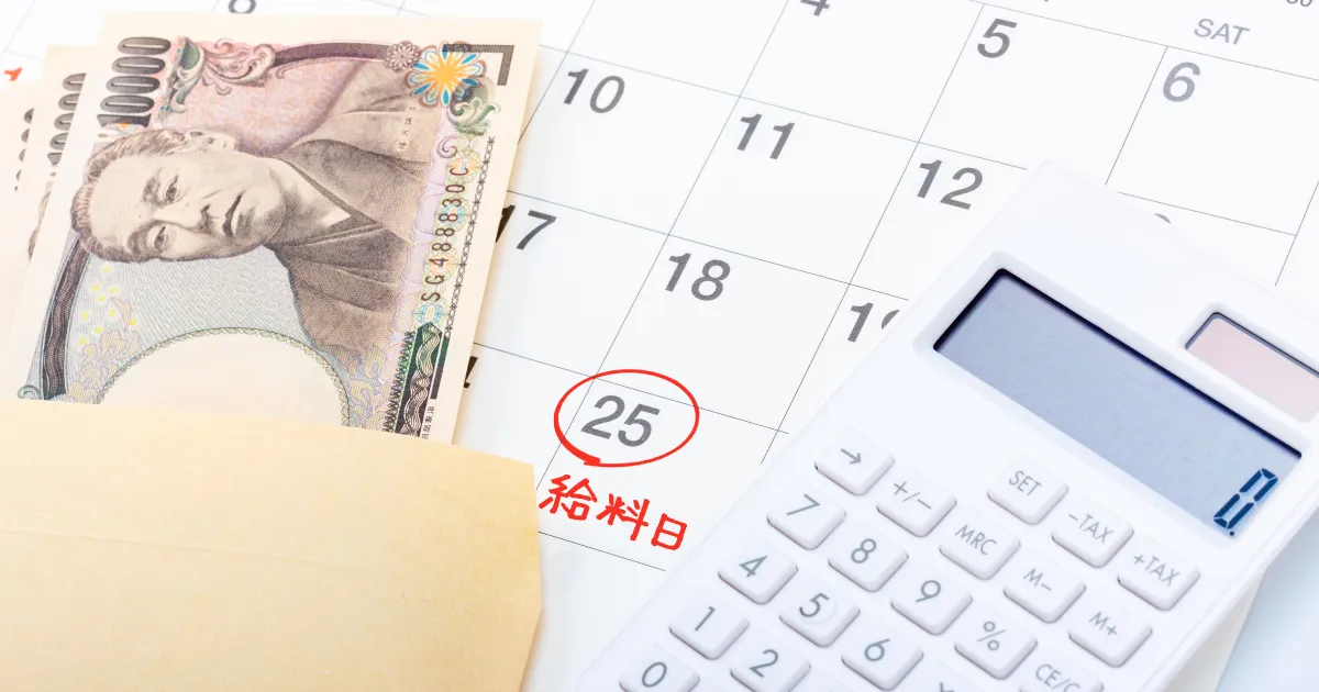 給料日を示すカレンダーと封筒に入った現金、電卓が並べられた画像。給与計算や支払いをイメージした構図。