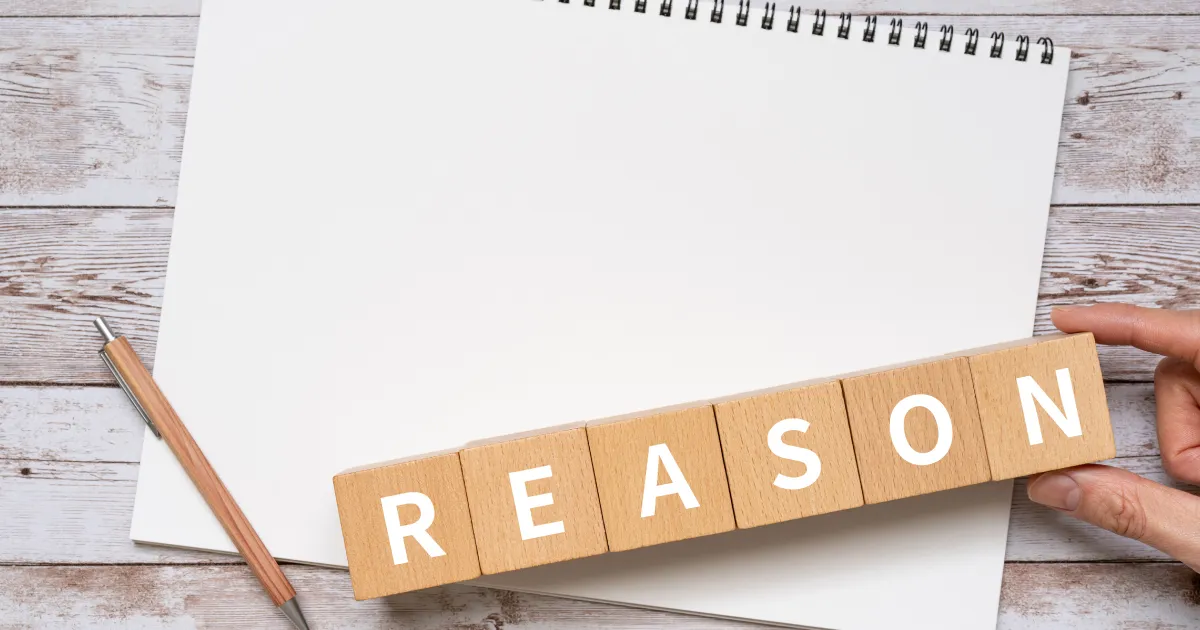 木製ブロックに『REASON』と書かれた文字と白いノート - ガクチカを企業が聞く理由を説明するセクションのイメージ