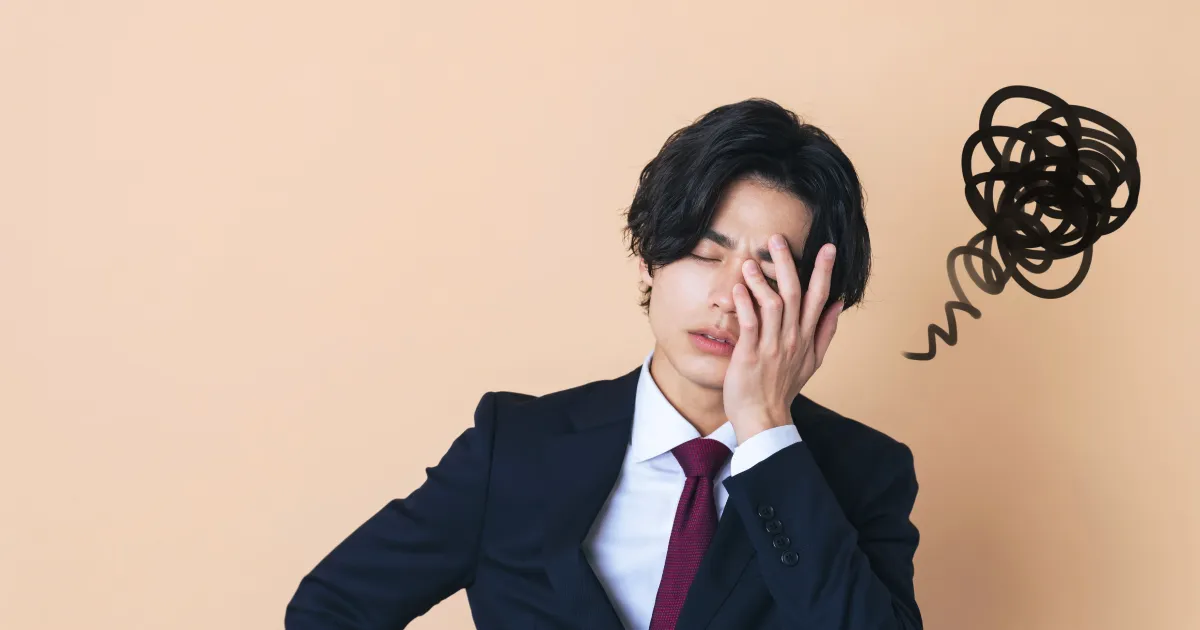 スーツ姿の男性が顔に手を当てて悩んでいる様子。背景には黒いぐるぐる模様が描かれ、ストレスや不安を象徴している。就活ストレスを抱える人の特徴を表現したイメージ。
