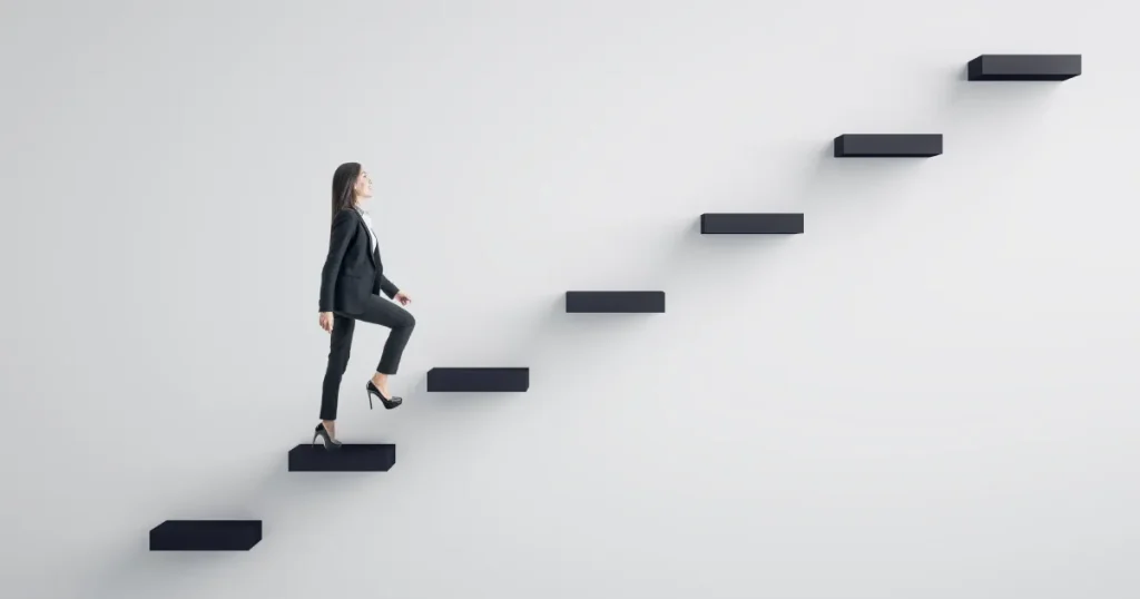 スーツ姿の女性が階段を一歩ずつ上がる様子。転職活動の基本的な流れを象徴するイメージ。