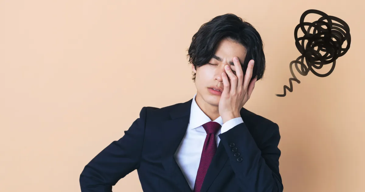 スーツ姿の男性が悩んだ表情で顔に手を当てている様子。背景に描かれた黒いもやもやが、自己分析で自分の強みが見つからない就活生の葛藤を象徴。