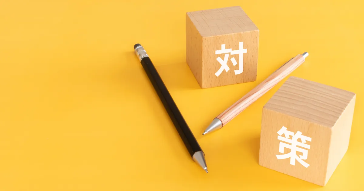 黄色の背景に置かれた『対策』と書かれた木製ブロックと2本のペン。転職面接で逆質問の準備をするための対策を象徴する画像。