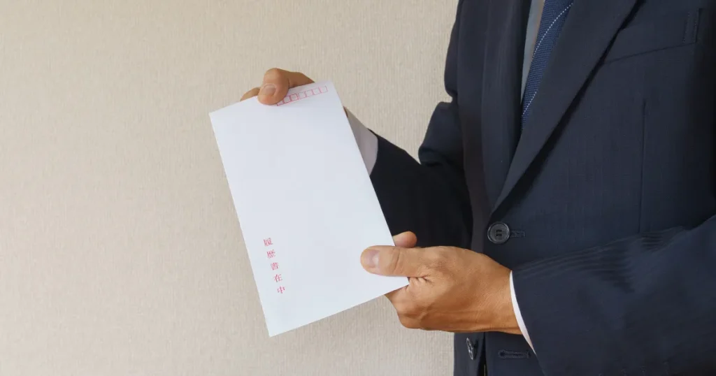 スーツを着た男性が『履歴書在中』と記載された封筒を持っている様子。