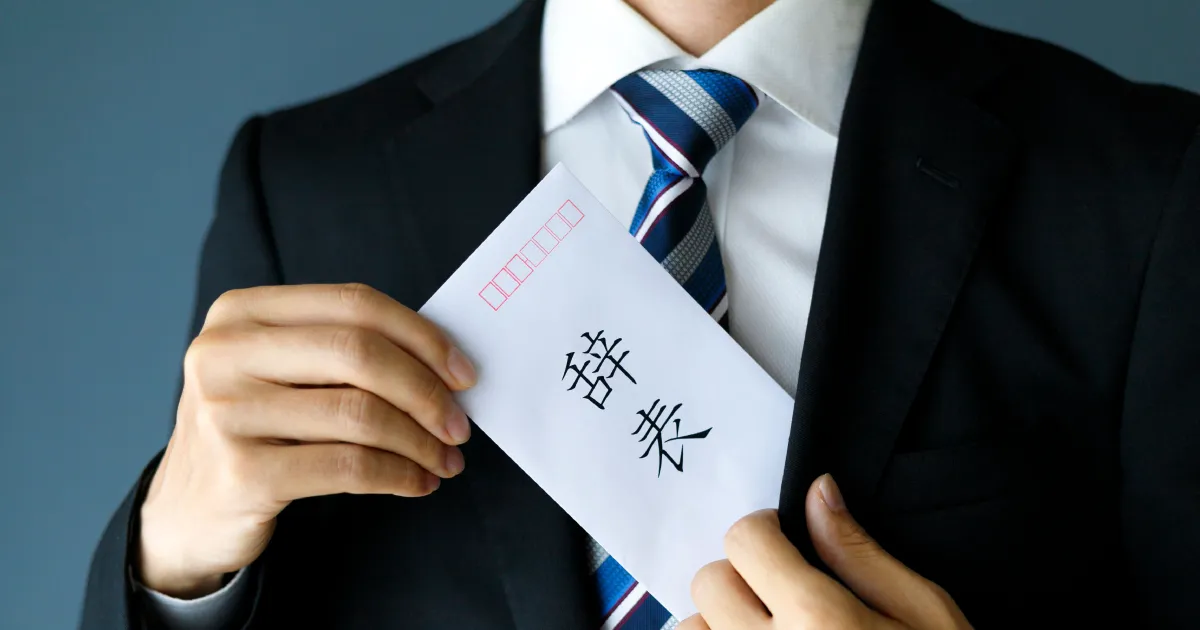 スーツを着た男性が『辞表』と書かれた封筒を持っている様子。辞表の提出を示すイメージ。