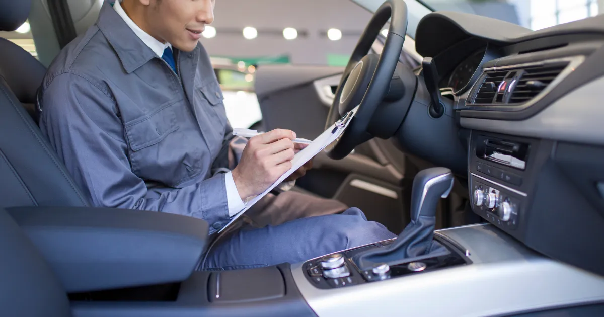 車内で点検リストを確認しながら作業を進める自動車整備士。車両のメンテナンス作業を行う様子。