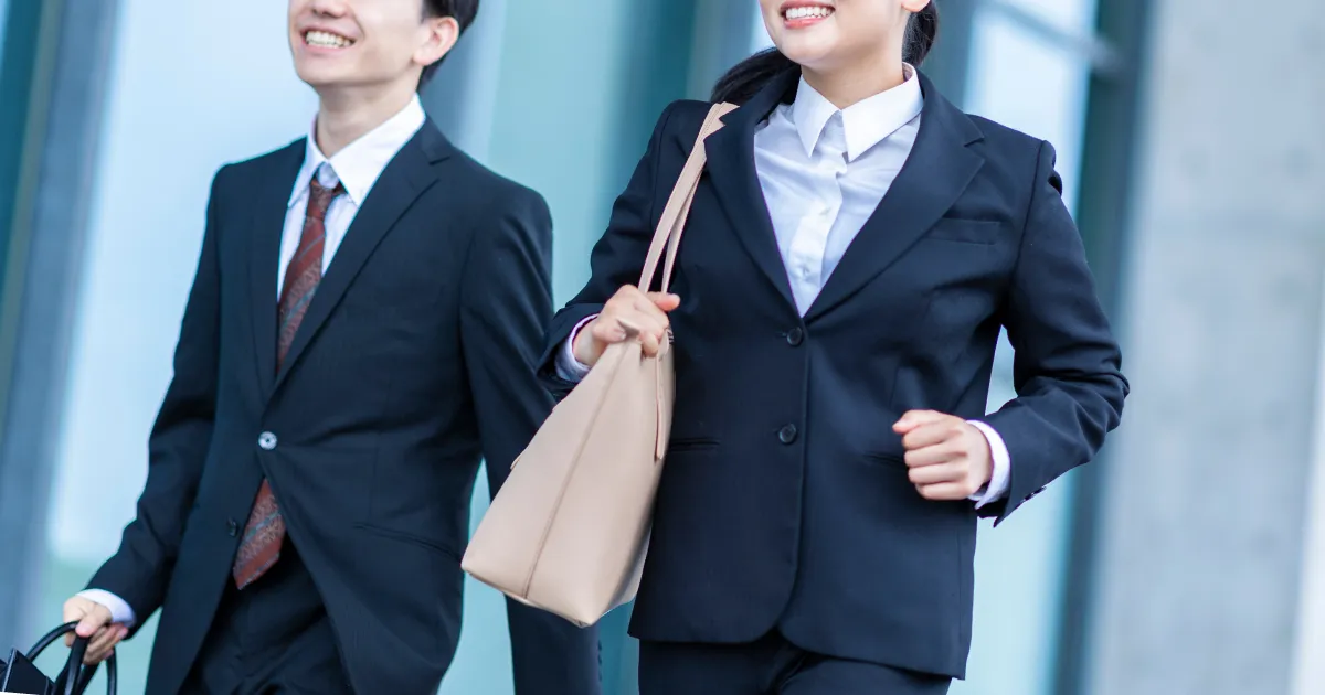 スーツを着た就活生の男女が笑顔で歩いている様子。自己分析を通じて自分の強みを把握し、就活に自信を持って臨む姿を示すイメージ。
