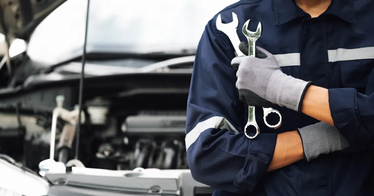 車のボンネット前で工具を持つ自動車整備士。自動車整備士の就職先をイメージした写真。
