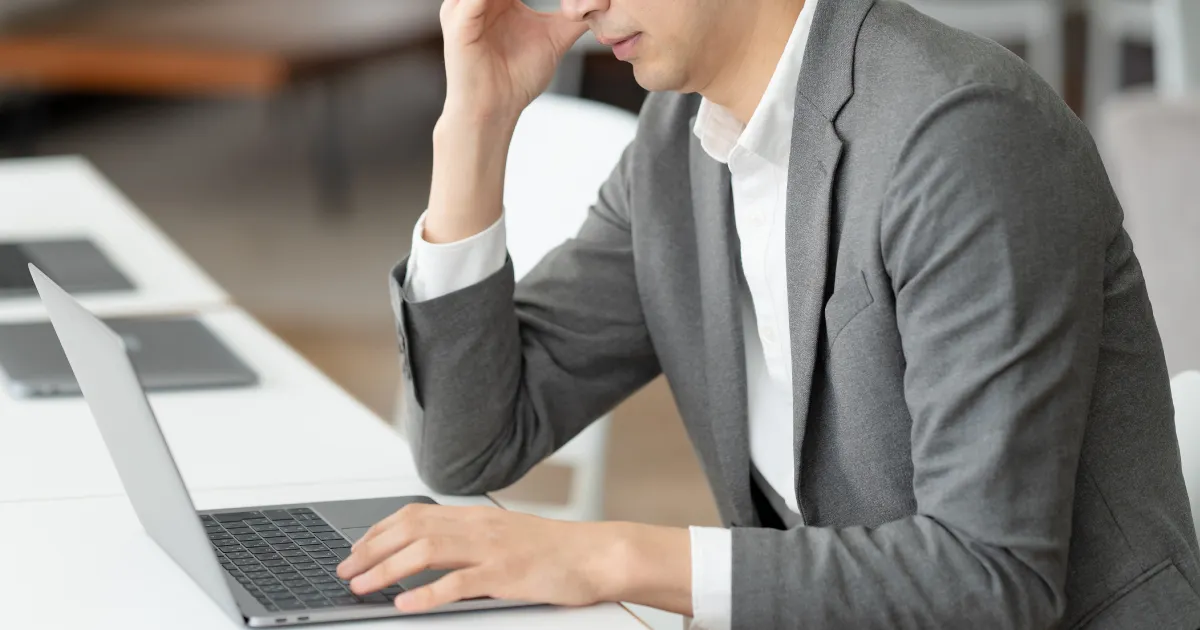 ノートパソコンの前で頭を抱えるスーツ姿の男性。転職で『自分に合う仕事が見つからない』と悩む原因について説明するセクションを象徴する画像。