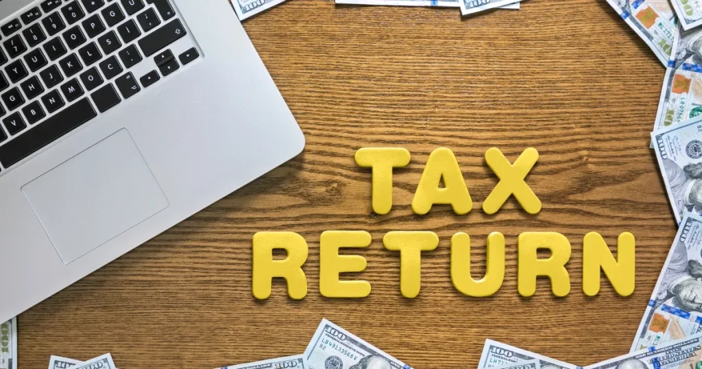 木製テーブルに置かれた『TAX RETURN（確定申告）』の文字とノートパソコン。転職後に確定申告が必要となる事例を説明するイメージ。