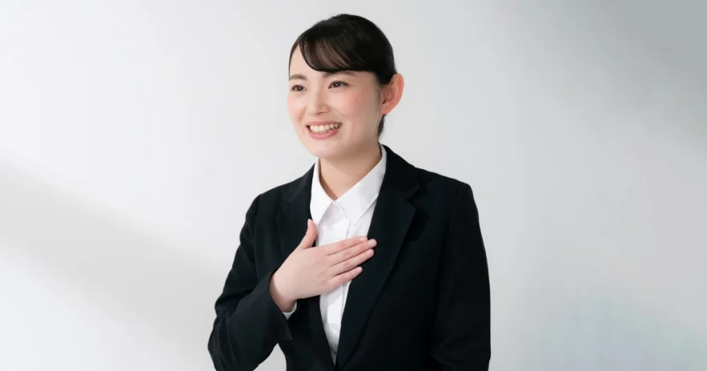 面接で好印象を与える女性 - 清潔感のある髪型とスーツ姿で胸に手を当てて笑顔を見せる