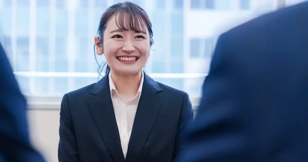 面接中に笑顔で答えるスーツ姿の女性。自信を持って志望理由を伝える様子を描写した画像で、『志望理由の伝え方』セクションに使用されています。