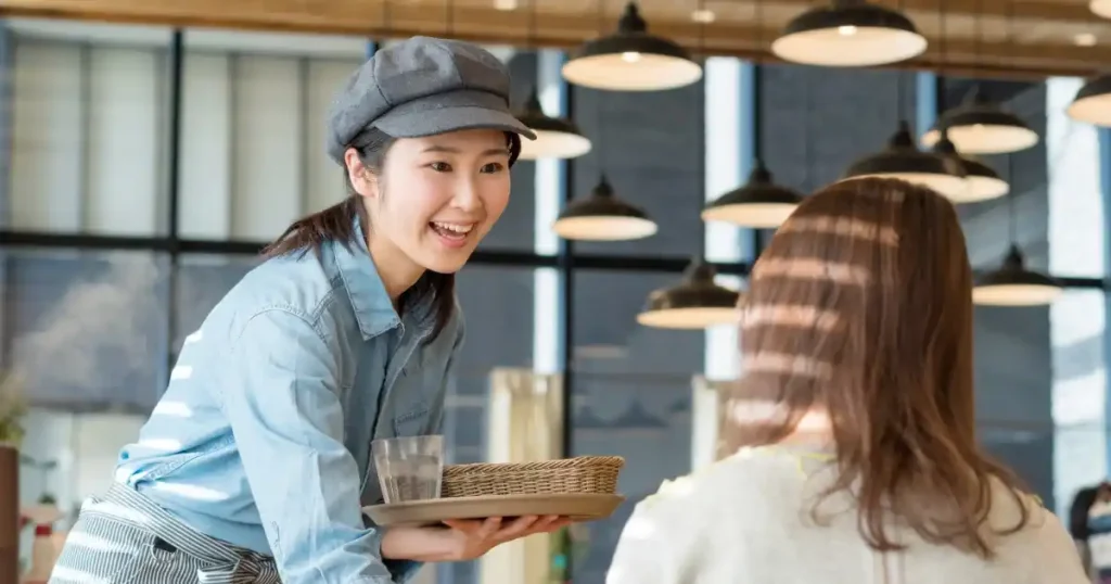 飲食店のホールスタッフが笑顔で接客している様子。キャリアパスの一環としてアルバイトから正社員への成長を象徴するシーン。