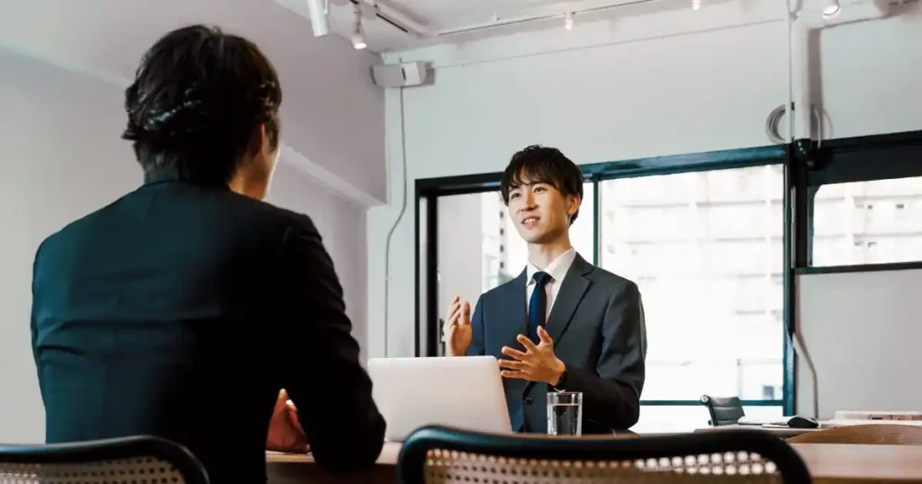 スーツを着た男性が面接官に向かって自信を持って話している様子 - ガクチカの探し方について説明するセクションのイメージ
