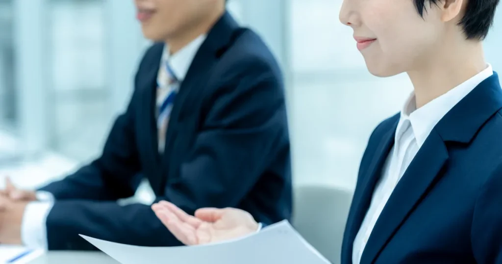 スーツを着た就活生が面接官と笑顔で向き合う様子 - 面接で採用担当者に好印象を与える話し方を解説するセクションのイメージ