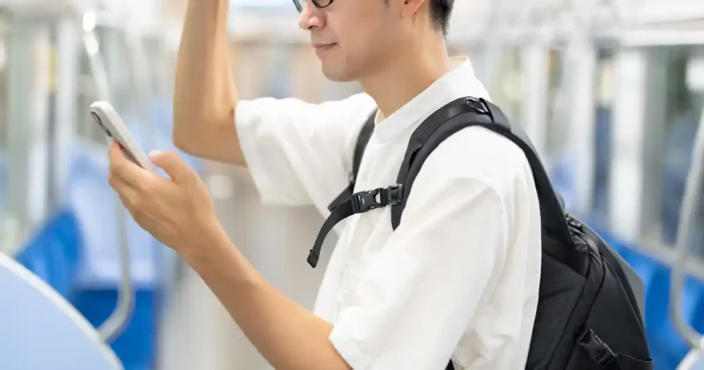 電車内でスマートフォンを操作するバックパックを背負った男性 - フリーターから転職が難しい理由を解説するセクション
