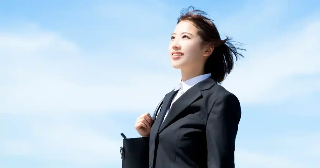 スーツを着て晴れた空の下で笑顔を見せる就活中の女性 - 面接当日に必ず持参すべきアイテムを説明するセクション用の画像