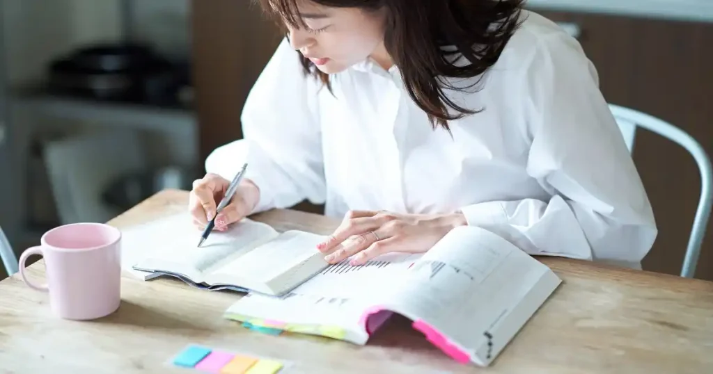 資格取得の勉強をする女性 - デスクで本を開き、メモを取りながら集中して学習する様子