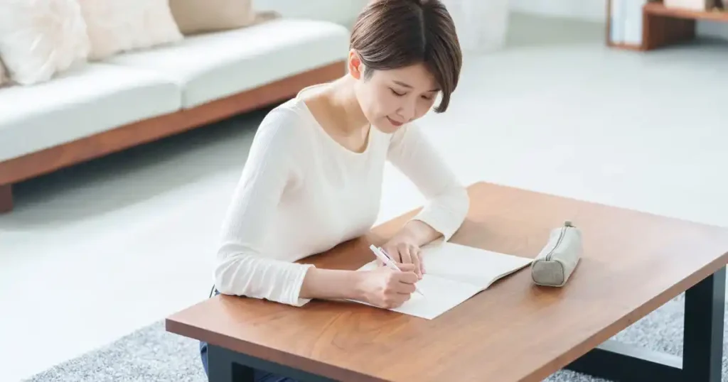 リビングのテーブルでノートに自己PR文を書き込む女性 - 採用担当者の印象に残る自己PR文を書くコツを説明するセクションのイメージ
