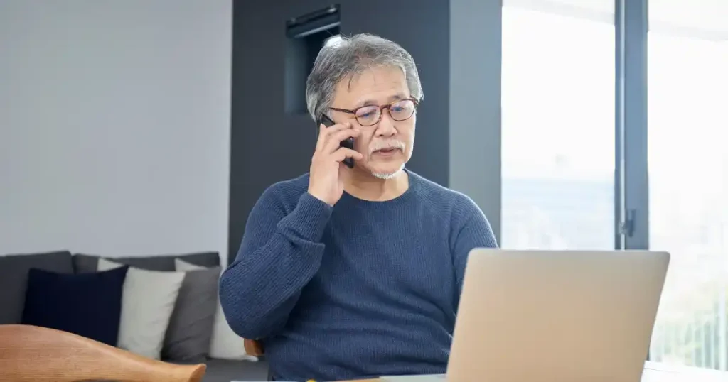 パソコンを見ながら電話で話しているシニア男性 - シニア層の雇用に関する制度の説明に関連したイメージ