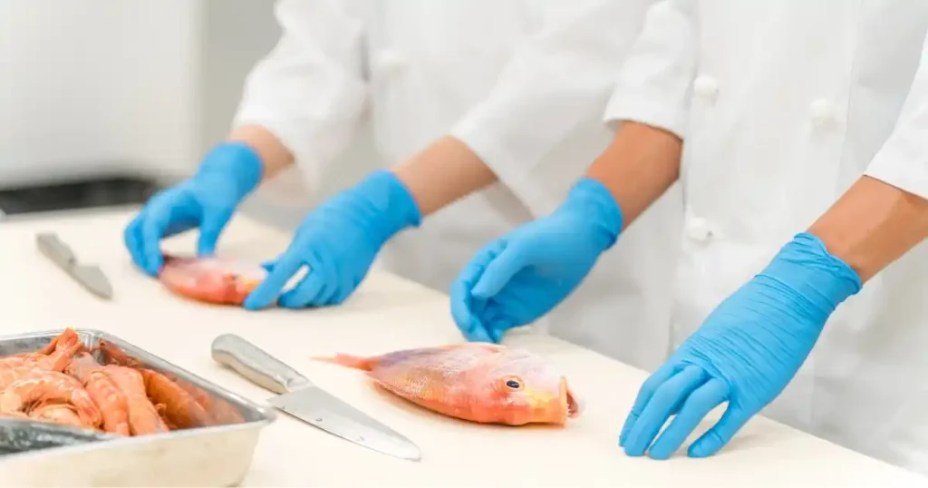 寿司学校の実習風景 - 青い手袋を着用した生徒が魚を捌いている様子