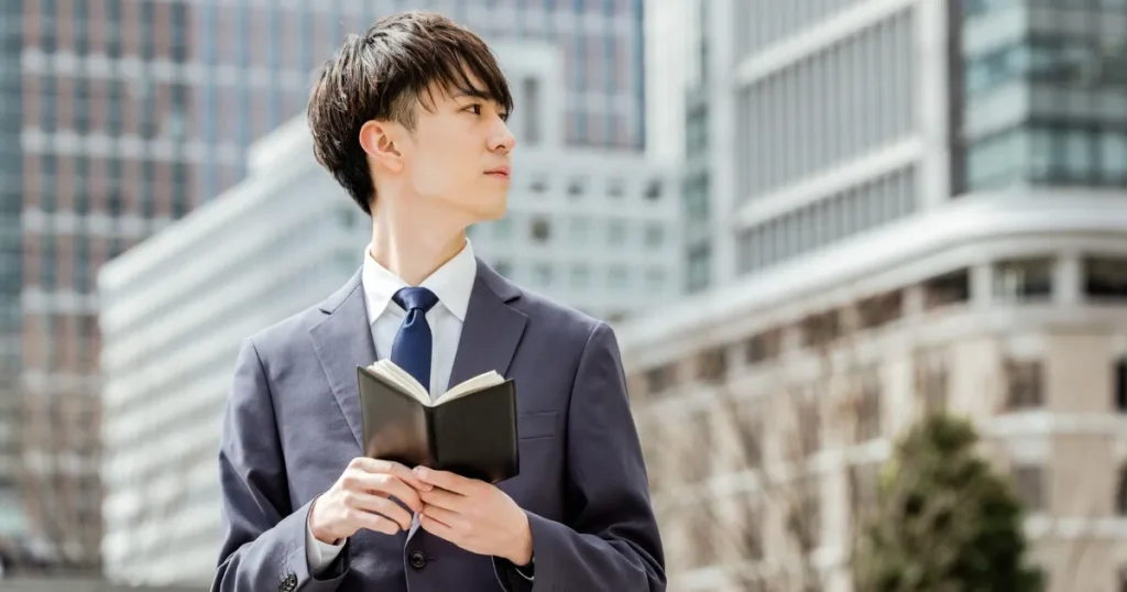 スーツ姿で手帳を持つ男性 - 新卒が社会人デビューを成功させるための必須アイテムを象徴するイメージ