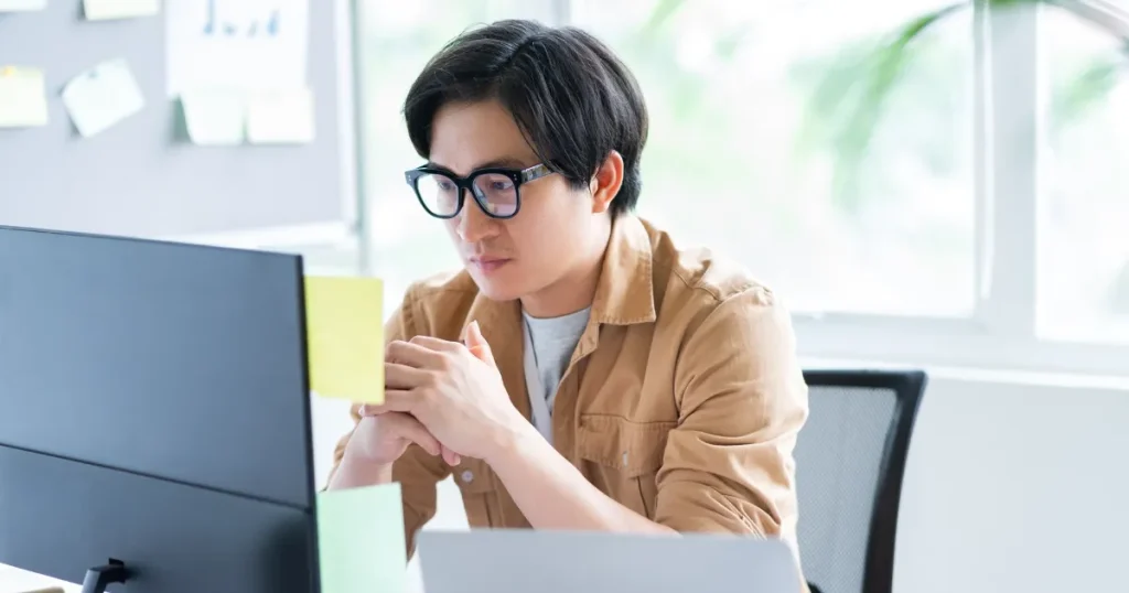 パソコンの画面を真剣に見つめるメガネをかけた男性。Webテスト本番前の準備に集中している様子を表現したイメージ。