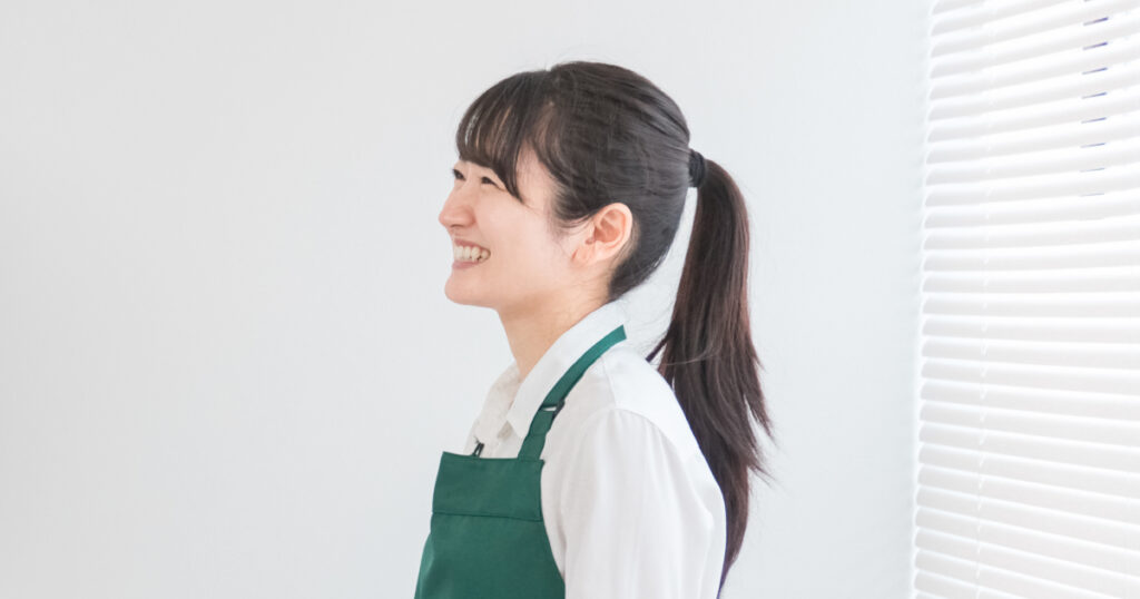 笑顔の女性スタッフがエプロンを着用して横を向いている姿。青果専門店で働くために必要なスキルを象徴するイメージ。