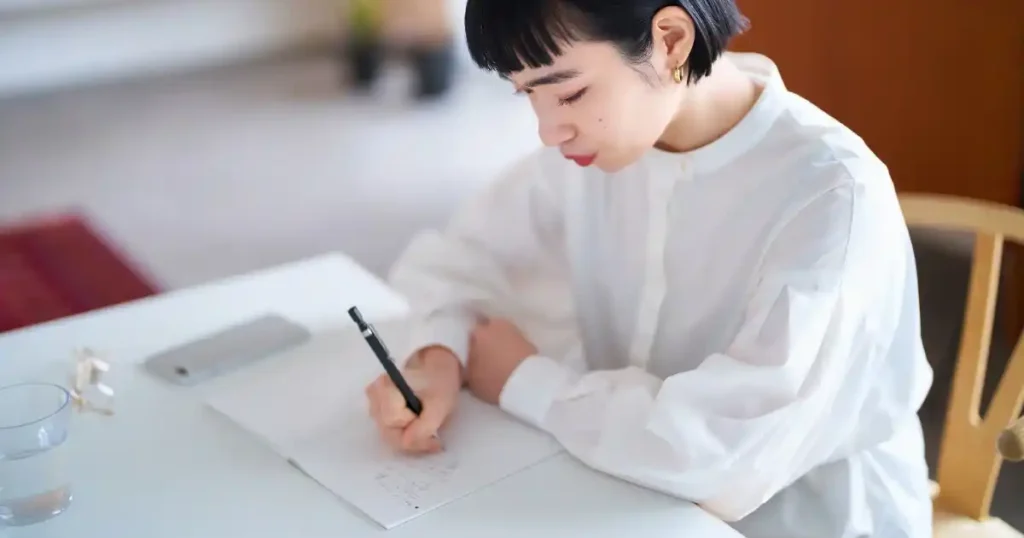 机に向かいノートに書き込みをしている女性。自己分析のフレームワークを用いて強み弱みを整理している様子。
