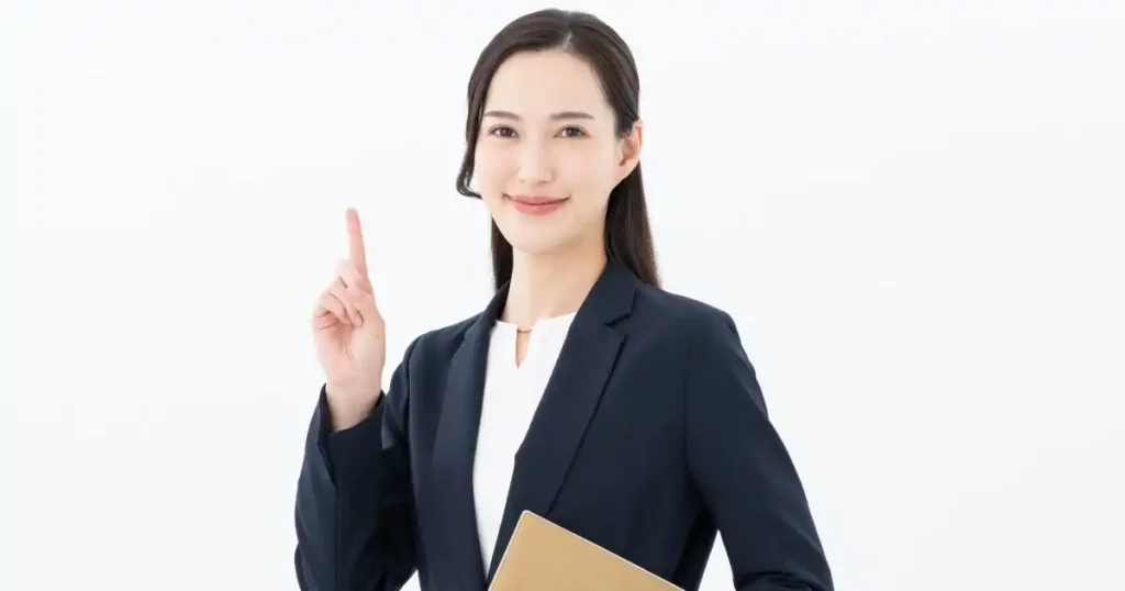 スーツ姿の女性が指を立ててポイントを示しながら微笑んでいる様子。