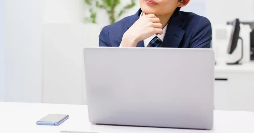スーツ姿で机に座り、ノートパソコンを前に考え込む男性。休職中の退職について調べたり検討したりしている様子。