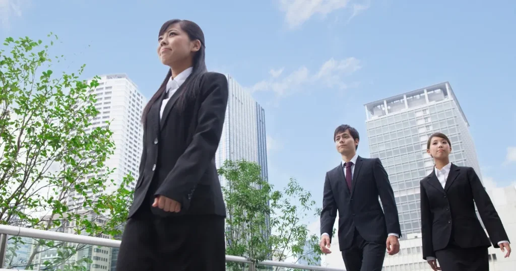 スーツを着た若い男女が都会の背景を背に前を向いて歩く様子 - インターンシップで採用担当者に好印象を与えるポイントを象徴するイメージ