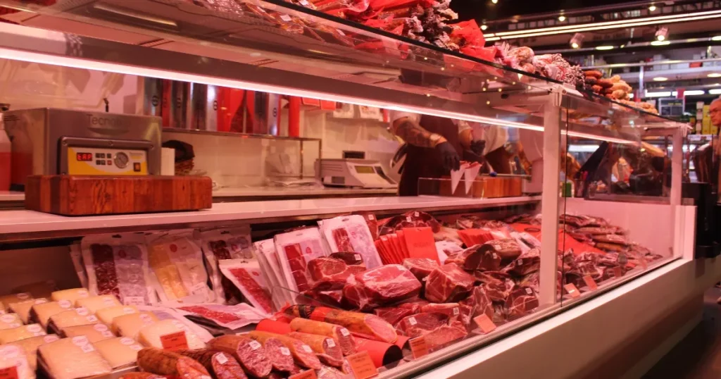精肉店のショーケースに並ぶ新鮮な肉製品。背景には店員が作業する様子が見られ、精肉店の業務内容を示すイメージ。