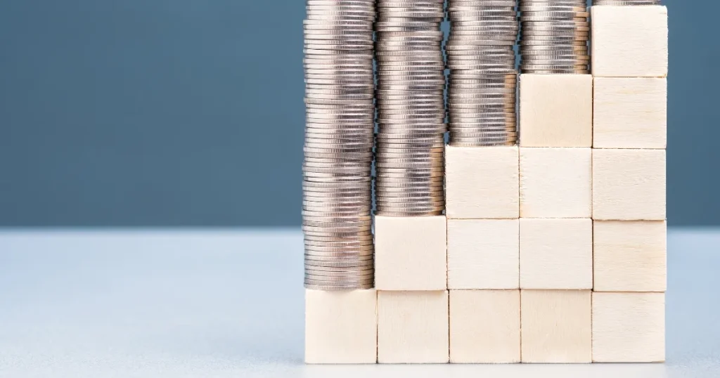 積み上げられたコインと木製ブロック - 補助金・助成金制度を活用するメリットを象徴するイメージ