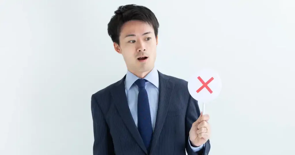 スーツを着た男性が赤いバツ印を示す札を持つ姿。転職面接で避けるべき逆質問のNGパターンについて説明するセクションを象徴する画像。