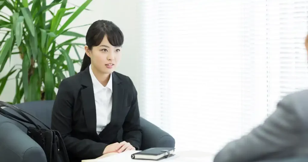 リクルーター面談に必要な持ち物について説明するセクションのイメージ。スーツを着た女性が面談中で、テーブルの上にはメモ帳とペンが置かれている。