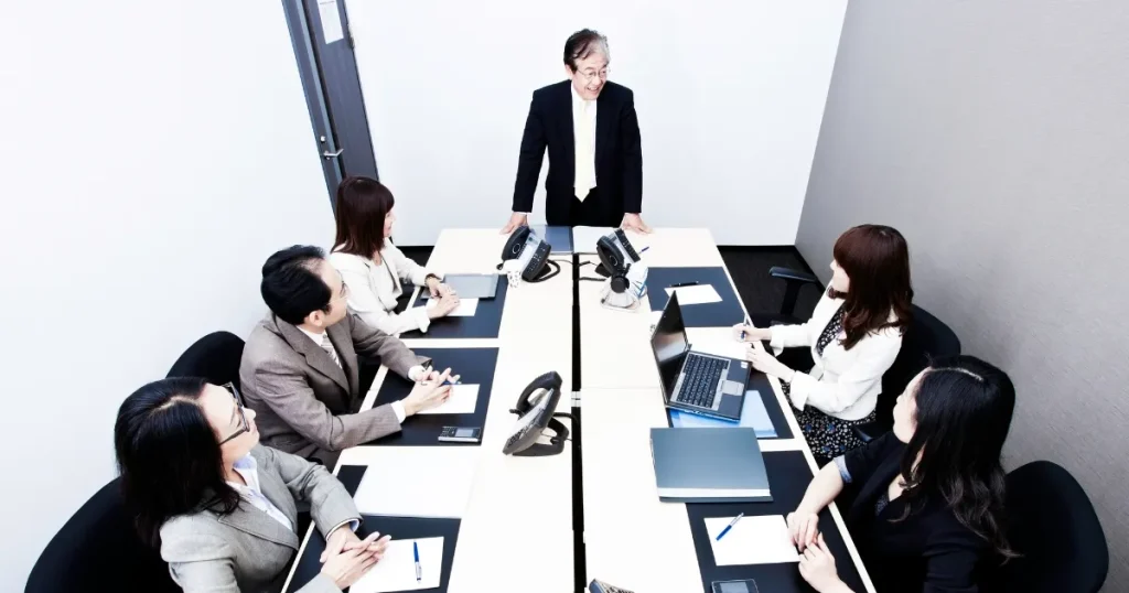 会議室で座談会形式の打ち合わせをしている様子。机を囲む参加者たちがメモを取り、話に耳を傾けている。