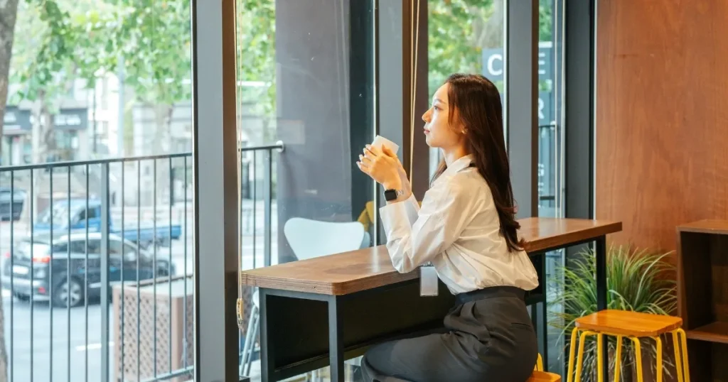 カフェのカウンター席で窓の外を眺めながらコーヒーを飲む女性。退職前に有給休暇を使い切れず泣き寝入りしないためのポイントについて説明するセクション用の画像。