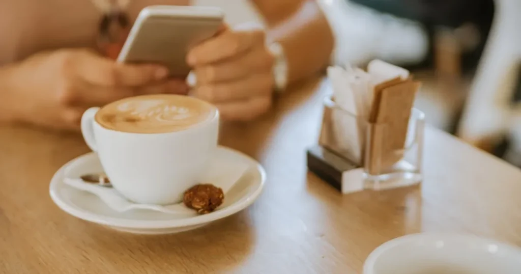 カフェのテーブルに置かれたラテアートが施されたコーヒーカップ。背景にはスマートフォンを操作する手が写っている。有給休暇取得に関するQ&Aを説明するセクションのイメージ。