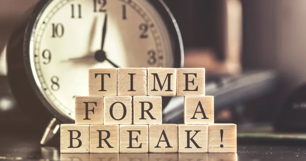 デスクの上に置かれたアナログ時計と『TIME FOR A BREAK!（休憩の時間！）』と書かれた木製ブロック。有給休暇中にやるべきことについて説明するセクションのイメージ。