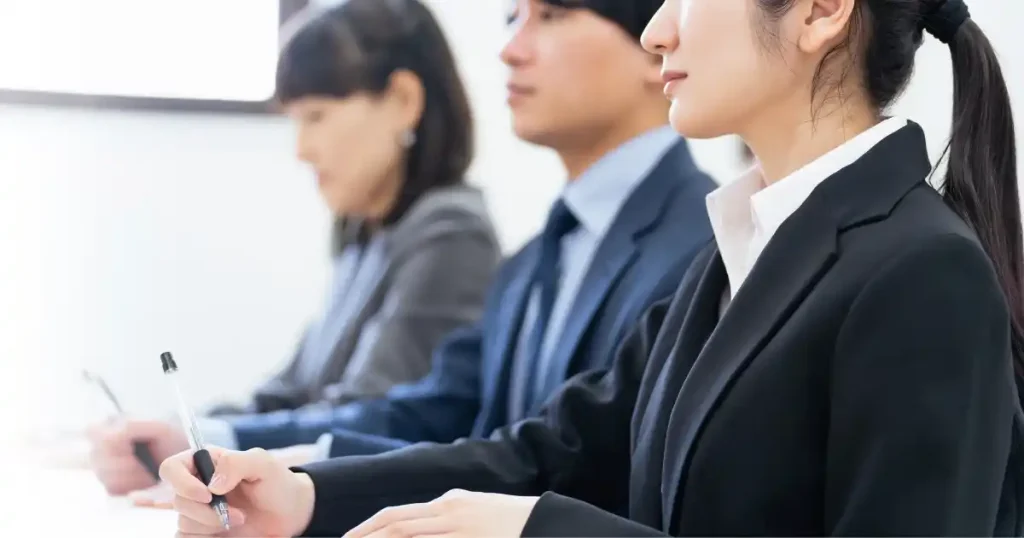 スーツ姿で真剣に話を聞きながらメモを取る学生たち。就職イベントの参加風景を象徴するイメージ。