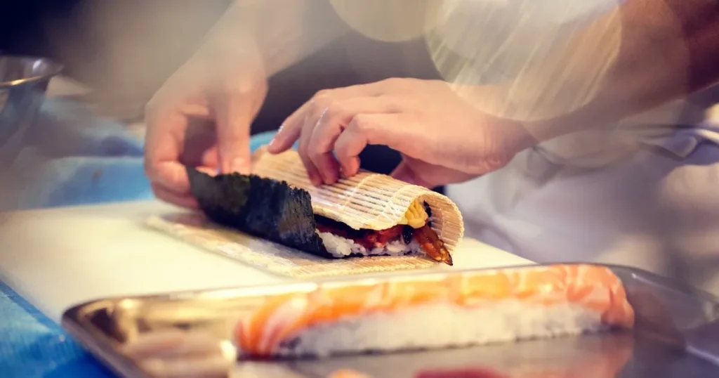寿司店で巻き寿司を作る手元の様子。巻きすを使いながら丁寧に仕上げている場面。