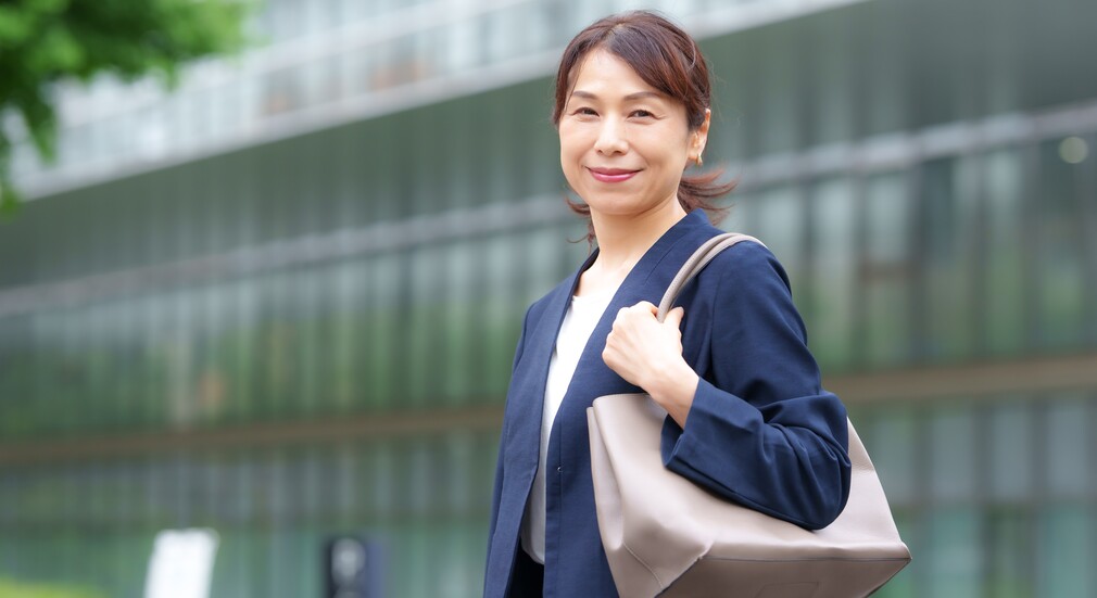 外を背景に笑顔で立つビジネスカジュアル姿の女性。50代転職を成功させるためのポイントを象徴するイメージ。