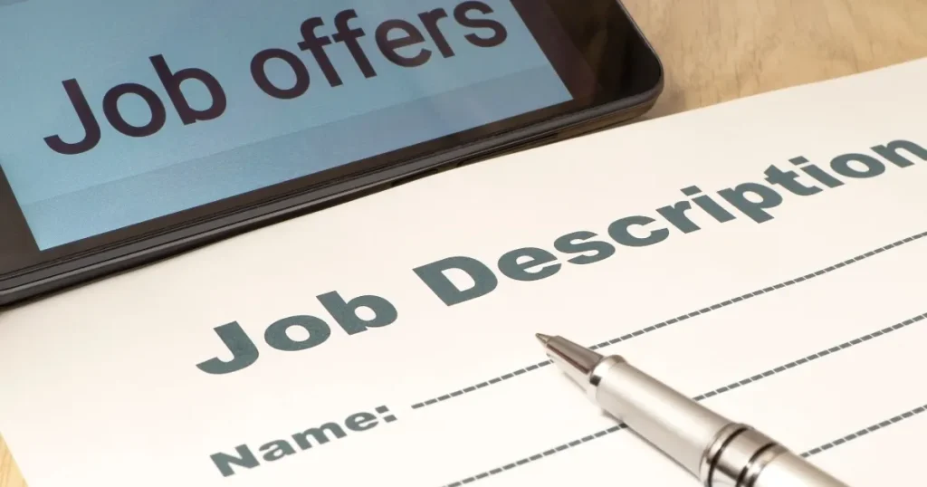 「Job Description」と書かれた求人票とペン、隣に「Job Offers」と表示されたスマートフォンが置かれた場面。求人票の概要を説明するイメージ。