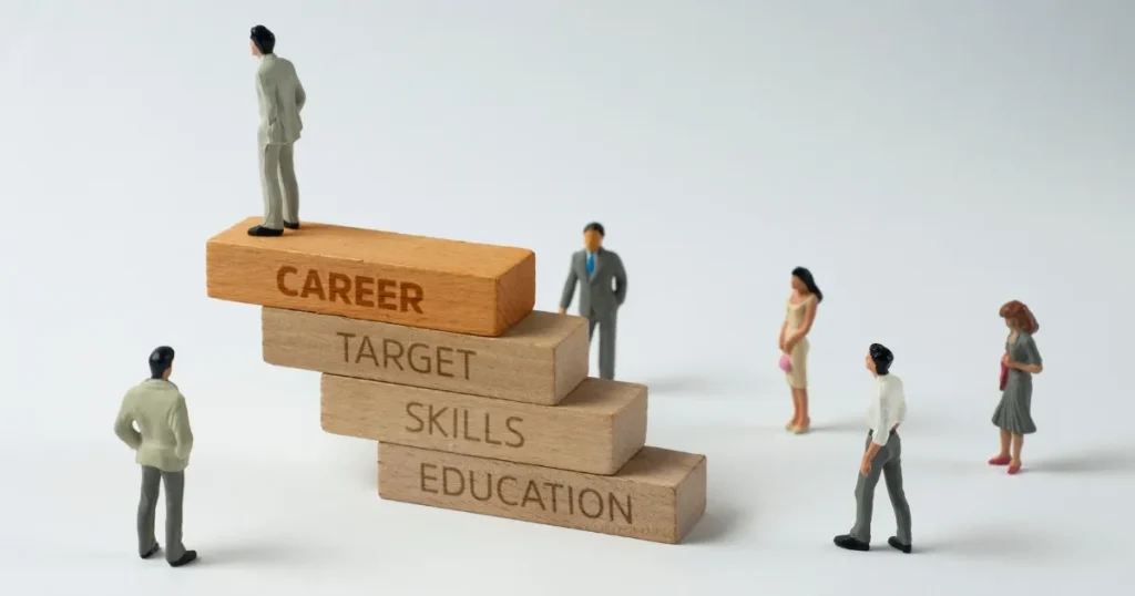 「EDUCATION」「SKILLS」「TARGET」「CAREER」と書かれたブロックで構成された階段の上に立つ人物。周囲には他の人物が集まり、キャリア形成のプロセスを象徴的に表現。