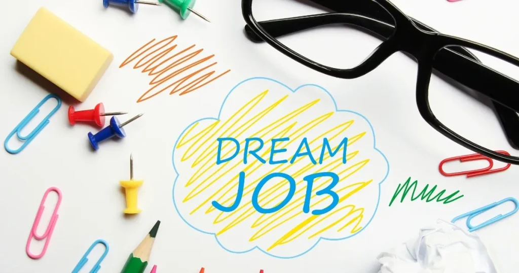 文房具やメガネが並ぶデスクに「DREAM JOB」と書かれたイラスト：理想の仕事に向けた志望動機を考えるプロセスを象徴するビジュアル。