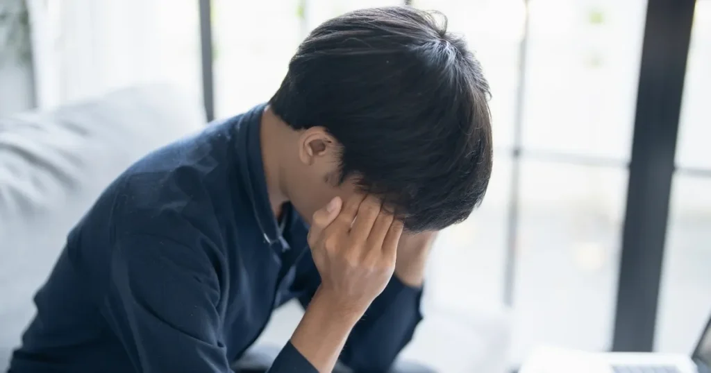 頭を抱えて悩んでいる男性。転職に対する不安や恐怖を感じている様子を表現したイメージ。